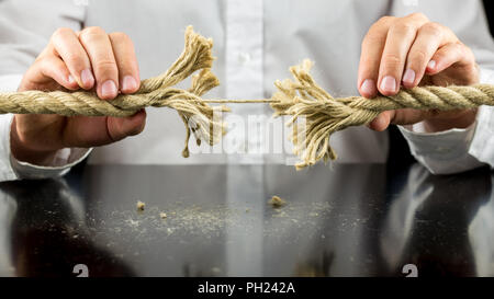 Mann hält ein ausgefranstes Seil mit einer der verbleibenden String in seine beiden Hände in die Gefahr und Not Konzept intakt. Stockfoto