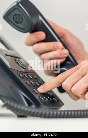 Einblick in die Hände eines mit seinem Finger in der Zahlen auf dem Tastenfeld in einer Kommunikation zu lochen Mann heraus wählen auf ein Festnetz Telefon Instrument Stockfoto