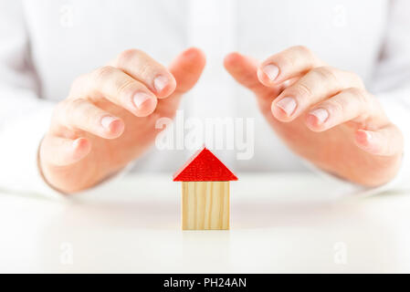 Männliche Hände abdecken und Schützen von einem kleinen hölzernen Modell eines Hauses oder Home Konzept des Eigentums, Sicherheit, Versicherung und Sicherheit Stockfoto