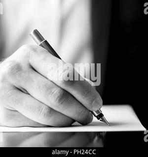 Niedrigen winkel schwarz-weiß Bild von einer männlichen Hand mit einem Füllhalter, als wenn das Schreiben auf ein leeres Blatt Papier mit flachen dof im quadratischen Format. Stockfoto