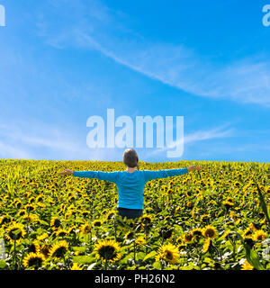 Junge Frau steht in der Mitte der Sonnenblume Feld mit Arme weit offen. Stockfoto