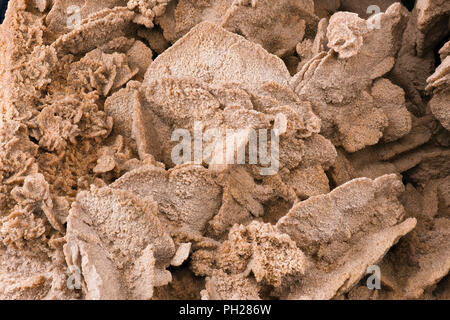 Rosa-roter Sand stieg aus der Nähe auf, Details der Sandkörner und die einzigartige Struktur einer Wüstensandrose, zarte Struktur dieser natürlichen Formation Stockfoto