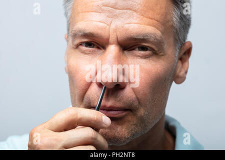 Porträt eines reifen Mannes Nase Zupfen der Haare mit einer Pinzette Stockfoto
