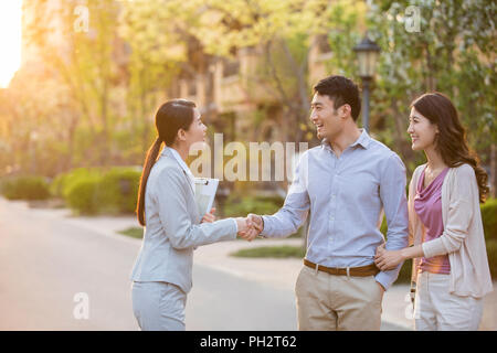 Glückliches junges Paar Hände schütteln mit Realtor Stockfoto