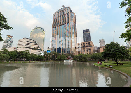 Blick auf einen Teich und viele Menschen in der Benchasiri Park und moderne Gebäude hinter dem Park in der Innenstadt von Bangkok, Thailand. Stockfoto