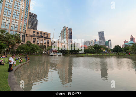 Blick auf einen Teich und viele Menschen in der Benchasiri Park und moderne Gebäude hinter dem Park in der Innenstadt von Bangkok, Thailand. Stockfoto