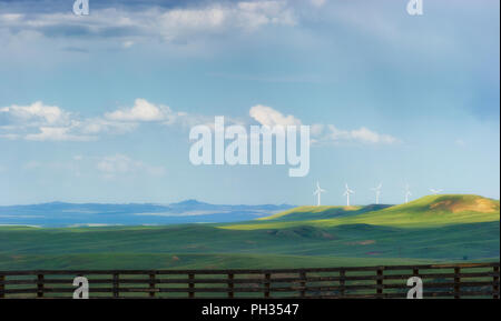 Blick auf die Wyoming offene Landschaft von der Autobahn 80, in denen Windenergieanlagen auf Abstand Hügeln mit hölzernen Zaun im Vordergrund bei bewölktem Himmel stehen gesehen. Stockfoto