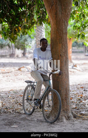 OUSSOUYE, SENEGAL - Apr 30, 2017: Unbekannter senegalesischen Mann reitet ein Fahrrad im heiligen Wald in der Nähe von Kaguit Dorf Stockfoto