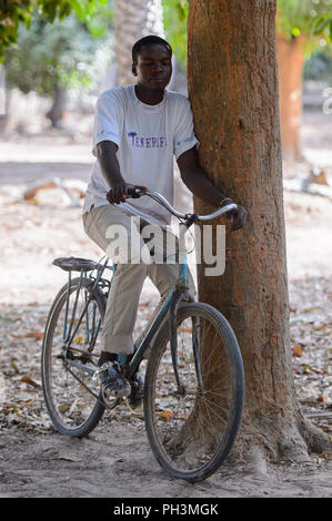 OUSSOUYE, SENEGAL - Apr 30, 2017: Unbekannter senegalesischen Mann reitet ein Fahrrad im heiligen Wald in der Nähe von Kaguit Dorf Stockfoto