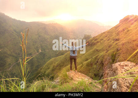 Sportliche Frau, die mit erhobenen Armen auf der Oberseite oh Hill suchen bei Sonnenaufgang. Stockfoto