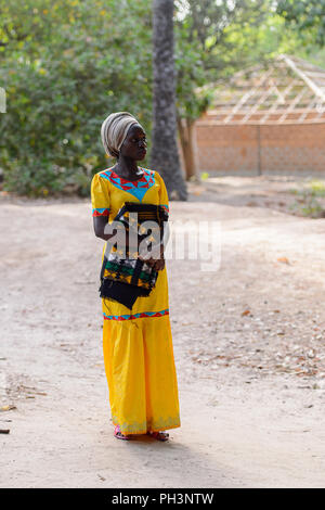 OUSSOUYE, SENEGAL - Apr 30, 2017: Unbekannter senegalesische Frau im gelben Kleid und beige Kopftuch hält farbigen plaid im heiligen Wald in der Nähe von Kag Stockfoto