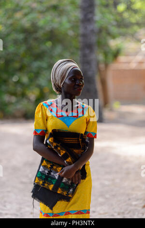 OUSSOUYE, SENEGAL - Apr 30, 2017: Unbekannter senegalesische Frau im gelben Kleid und beige Kopftuch hält farbigen plaid im heiligen Wald in der Nähe von Kag Stockfoto