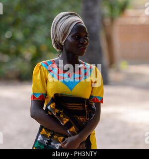 OUSSOUYE, SENEGAL - Apr 30, 2017: Unbekannter senegalesische Frau im gelben Kleid und beige Kopftuch hält farbigen plaid im heiligen Wald in der Nähe von Kag Stockfoto