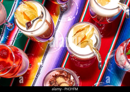 Schöne 2-in-1-Desserts aus Sahne, Beeren und Physalis, in dem hohe Weingläser mit einem Löffel stehen in einer Reihe auf einem lebendigen multicolor tablecl Stockfoto