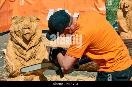 Erfahrene Tischler machen einen grossen Holz- Bär Skulptur mit einer Kettensäge bei einer lokalen Wettbewerb, fast fertig Stockfoto