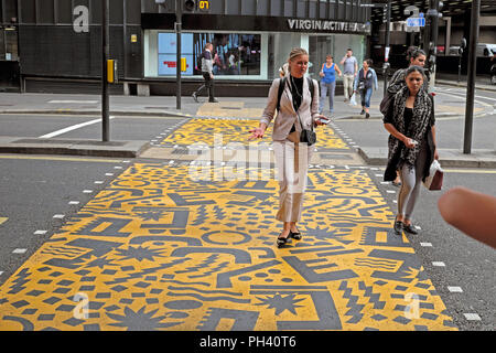 Kishimoto geometrische Grafik & junge Frauen zu Fuß auf der anderen Straßenseite gelb Fußgängerüberweg in der Nähe von Barbican Station in der Stadt London UK KATHY DEWITT Stockfoto
