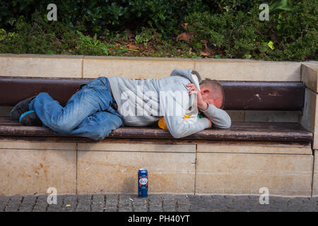 Mann der schläft liegend auf einer öffentlichen Bank, die möglicherweise betrunken und eingeschlafen sein, Bristol, Großbritannien Stockfoto