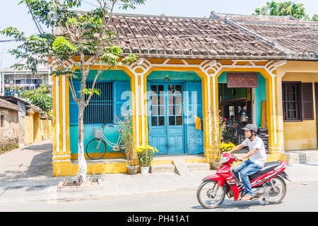 Hoi An, Vietnam - am 1. März 2010: ein Motorradfahrer fährt vorbei an einem typischen blauen Haus. Diese Art der Architektur in der Stadt Vororten. Stockfoto