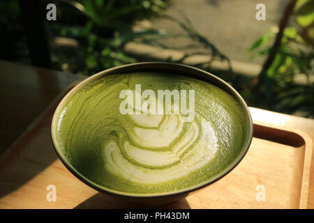 Eine Tasse heißen japanischen Matcha grüner Tee Latte in der Sonne mit unscharfen Pflanzen im Hintergrund Stockfoto