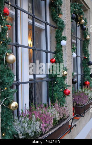Fenster, Blick von Außen, mit schönen Weihnachtsschmuck, Lichter, Kugeln, blühende heaathers, grüne Girlanden dekoriert. Stockfoto