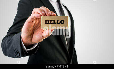 Nahaufnahme von Geschäftsmann mit einer kleinen rechteckigen hölzernen Schild, Hallo. Auf grauem Hintergrund. Stockfoto