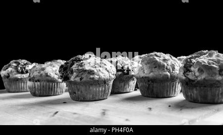 Schwarz-weiß Bild von einer Charge von frisch gebackene Muffins oder Cupcakes gegen einen dunklen Hintergrund mit Copyspace. Stockfoto