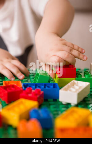 In der Nähe der Hände Kind spielen mit bunten Kunststoff Ziegel am Tisch. Kleinkind, das Spaß und Gebäude aus hellen Konstruktor Steine. Anfang l Stockfoto