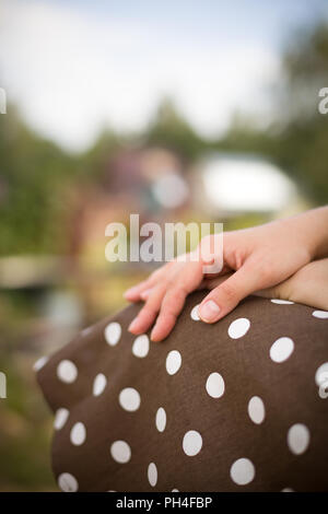 Die Frau, die Hände auf den Knien. Im Hintergrund. Braun gepunkteten Kleid. Stockfoto