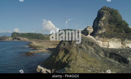 Natürliche Felsformation aus Kalkstein Stein an der Küste mit Windmühlen für elektrische Energie Produktion. Luftaufnahme von touristenattraktion Kapurpurawan Felsformation in Ilocos Norte, Philippinen, Luzon. Stockfoto