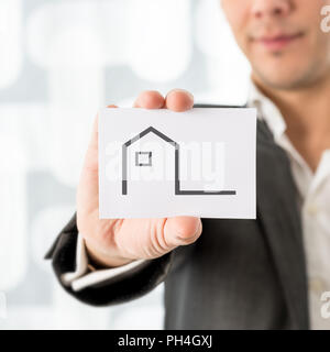 Unternehmer Halten eines Hauses Symbol auf einer Karte in einem konzeptionellen Bild von Immobilien, Agenten oder Makler, Eigentum oder Versicherung, bis der Karte schließen. Stockfoto