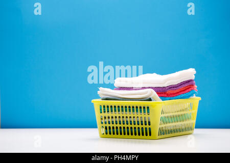 Foto von Stapel bunter Bettwäsche in Gelb Warenkorb auf leeren blauen Hintergrund. Stockfoto