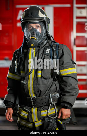 Foto von Feuerwehrmann in Gasmaske und Helm in der Nähe von Feuer Motor Stockfoto