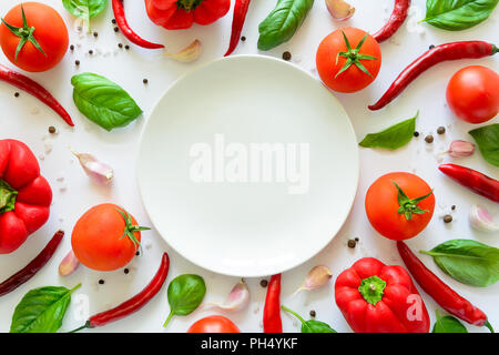 Bunte pizza Zutaten Muster aus Tomaten, Pfeffer, Chili, Knoblauch, Basilikum und leeren Teller auf weißem Hintergrund. Kochen Konzept. Ansicht von oben. Fla Stockfoto