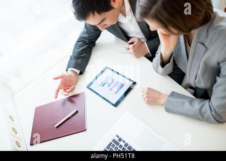 Hohe Betrachtungswinkel und einer jungen Geschäftsmann und Frau mit einem Brainstorming, wie sie sitzen zusammen an einem Schreibtisch im Büro über eine analytische Stockfoto