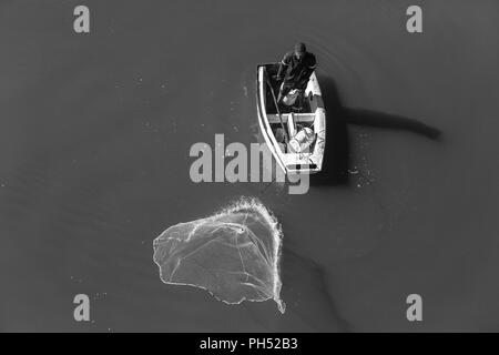 Fischer casting net Aktion, um die Fischerei mit kleinen Boot in Fluss Wasser der Lagune overhead Foto Stockfoto