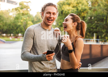 Bild von glücklich lachend Fitness Sport liebende Paar Freunde im Park im freien Musik hören mit Kopfhörern. Stockfoto