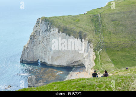 Ein paar setzte sich auf einem grasbewachsenen Steilküste auf einem sonnigen klaren Tag, bis zu einer Bucht von Fledermäusen den Kopf, in der Nähe der Durdle Door auf der Jurassic Coast South England Stockfoto