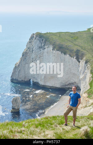 Im mittleren Alter Mann auf einem grasbewachsenen Cliff an einem sonnigen Tag, mit Fledermäusen Kopf hinter, in der Nähe der Durdle Door auf der Jurassic Coast South England Stockfoto