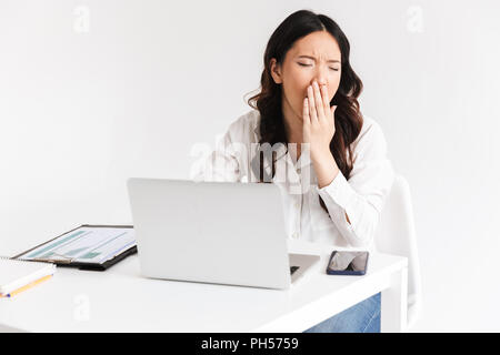 Foto von Überforderten müde Asian Business woman 20 s tragen Büro Kleidung Gähnen beim Sitzen am Tisch mit Laptop öffnen Über weiß isoliert backgro Stockfoto