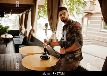 Stilvolle Bart 1001 Mann in Gläsern und militärischen Jacke rauchen Shisha an Street Bar. Arabische Modell Rest. Stockfoto