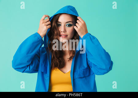 Foto der Europäischen junge Frau 20 s in Streetwear auf der Haube von Regenjacke oder Jacke über blauen Hintergrund isoliert Stockfoto