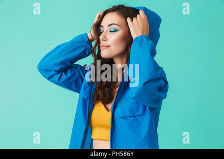 Foto von stilvollen junge Frau 20 s in Streetwear auf der Haube von Regenjacke oder Jacke über blauen Hintergrund isoliert Stockfoto