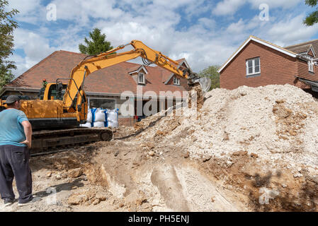 Ein Kettenbagger graben und Entfernen von Kalk zu einem Formular ein Graben für die Entwässerung equipmment auf einer Wohnsiedlung. Stockfoto