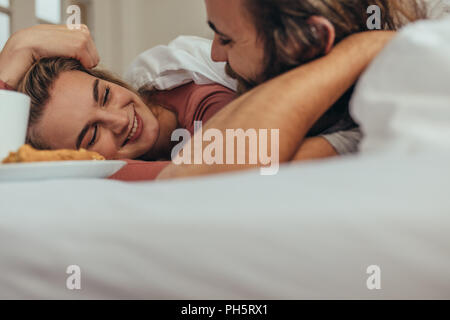 Lächelnd Mann und Frau schlafend auf dem Bett und an einander mit der Liebe. Paar liegend auf Bett unter einer Kuscheldecke mit Snacks auf dem Bett. Stockfoto