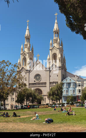 Die Menschen genießen Sie einen sonnigen Tag am Washington Square, mit der St. Peter und Paul Katholische Kirche im Hintergrund, San Francisco, Kalifornien, USA Stockfoto