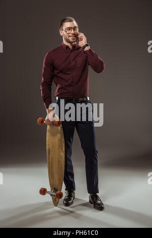 Lächelnder Mann mit Skateboard und Reden von Smartphone auf Schwarz Stockfoto