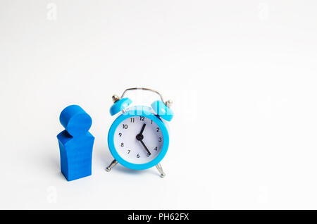 Ein Mann steht in der Nähe ein blauer Alarm Clock und wartet auf jemanden. Das Konzept der Wartezeit für ein Meeting, ein Datum. Spät und pünktlich. Die Kosten für die stündliche Arbeit o Stockfoto