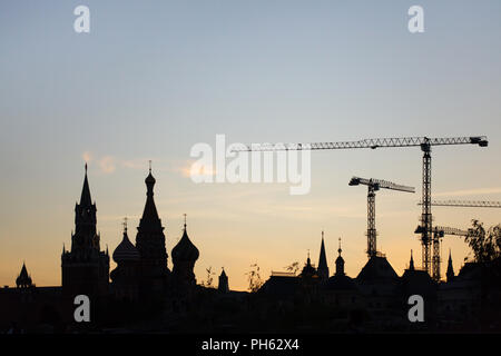 Sonnenuntergang über der Hebezeuge Krane neben die Basilius-Kathedrale auf dem Roten Platz und der Retter Spasskaja Turm (Turm) der Moskauer Kreml im Bild von zaryadye Park in Moskau, Russland. Stockfoto