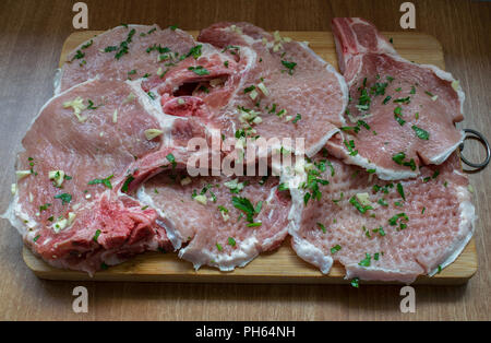 Draufsicht auf frisches rohes Schweinefleisch auf Schneidebrett mit Petersilie und Knoblauch fein hacken, bereit zum Kochen Stockfoto