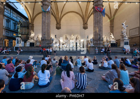 Florenz, Italien - 2018, Juli 14: Menschen sitzen auf dem Pflaster der Piazza della Signoria, bei einem Open-Air-Konzert in der Loggia dei Lanzi. Stockfoto
